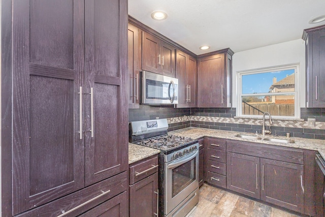 kitchen with light hardwood / wood-style flooring, sink, light stone counters, appliances with stainless steel finishes, and decorative backsplash