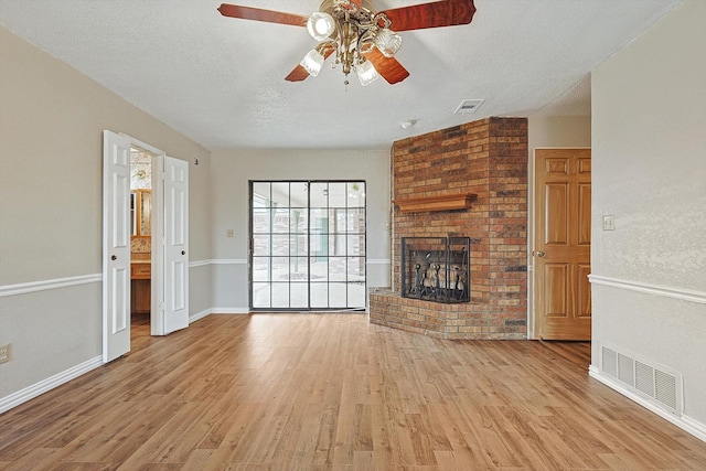 unfurnished living room with ceiling fan, a fireplace, light hardwood / wood-style floors, and a textured ceiling