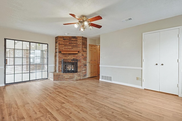 unfurnished living room with ceiling fan, a brick fireplace, a textured ceiling, and light wood-type flooring