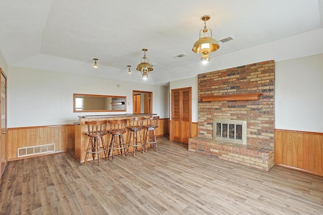 living room with wood walls, indoor bar, a raised ceiling, a brick fireplace, and light hardwood / wood-style flooring