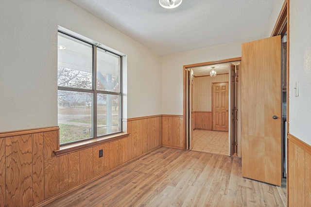 unfurnished room with wood walls, a textured ceiling, and light hardwood / wood-style flooring