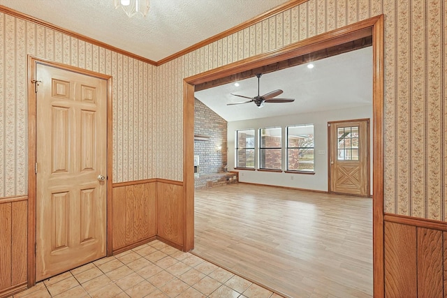 entrance foyer with a brick fireplace, a textured ceiling, light hardwood / wood-style flooring, ornamental molding, and ceiling fan