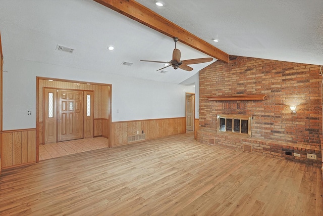 unfurnished living room featuring vaulted ceiling with beams, a textured ceiling, a brick fireplace, ceiling fan, and light hardwood / wood-style floors