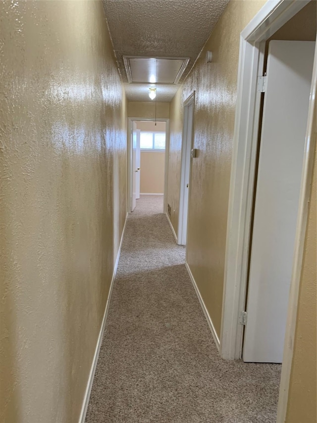 corridor with light colored carpet and a textured ceiling