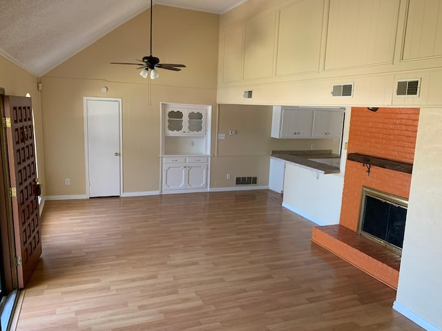 unfurnished living room with ceiling fan, high vaulted ceiling, a fireplace, and light hardwood / wood-style flooring