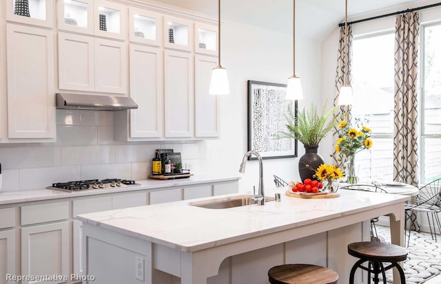 kitchen with decorative light fixtures, stainless steel gas stovetop, white cabinets, and a center island with sink