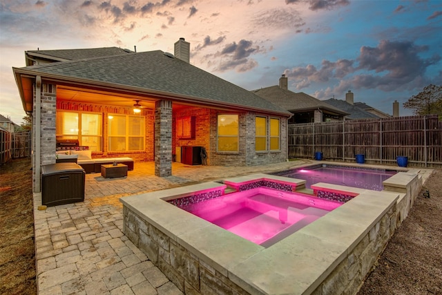 pool at dusk with an in ground hot tub, an outdoor living space with a fire pit, and a patio