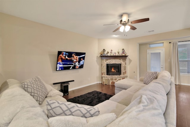 living room featuring ceiling fan, dark hardwood / wood-style floors, and a stone fireplace