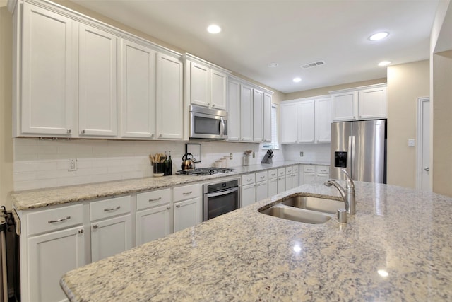 kitchen with light stone counters, sink, white cabinets, and stainless steel appliances