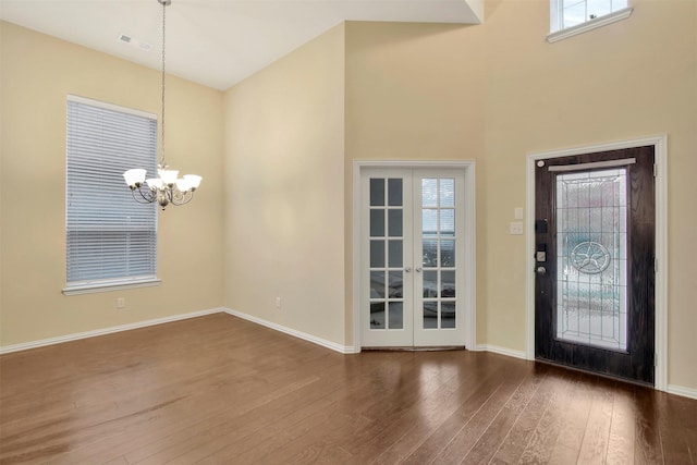 foyer entrance with a towering ceiling, french doors, dark hardwood / wood-style flooring, and a notable chandelier