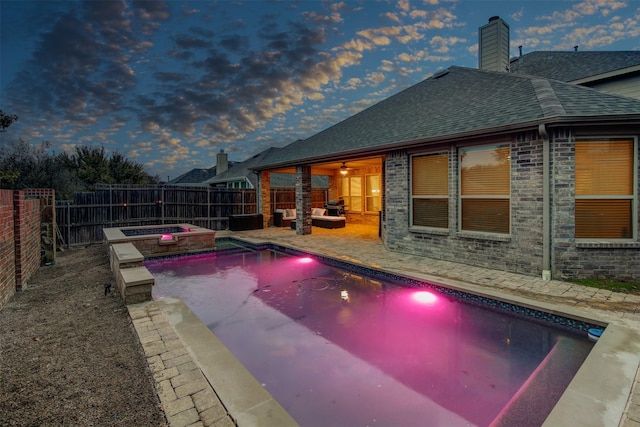 pool at dusk featuring an in ground hot tub, outdoor lounge area, and a patio