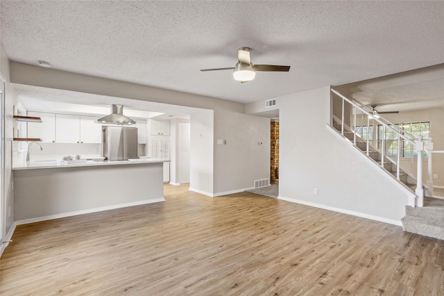 unfurnished living room featuring ceiling fan, sink, a textured ceiling, and light hardwood / wood-style flooring