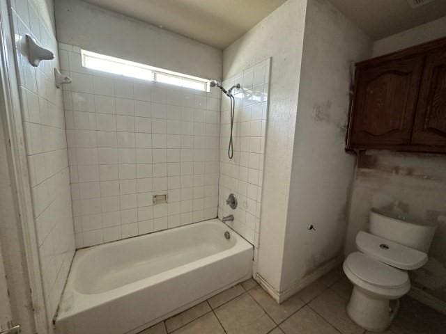 bathroom featuring tile patterned flooring, tiled shower / bath combo, and toilet