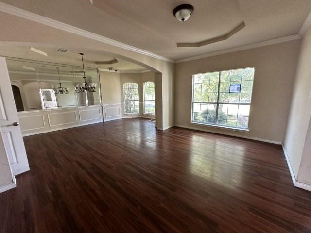 unfurnished room with ornamental molding, an inviting chandelier, a raised ceiling, and dark wood-type flooring