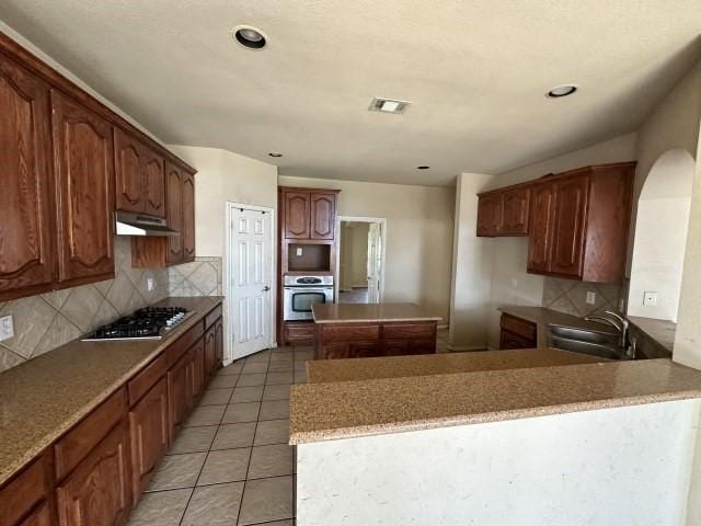 kitchen with sink, backsplash, stainless steel appliances, a center island, and tile patterned floors