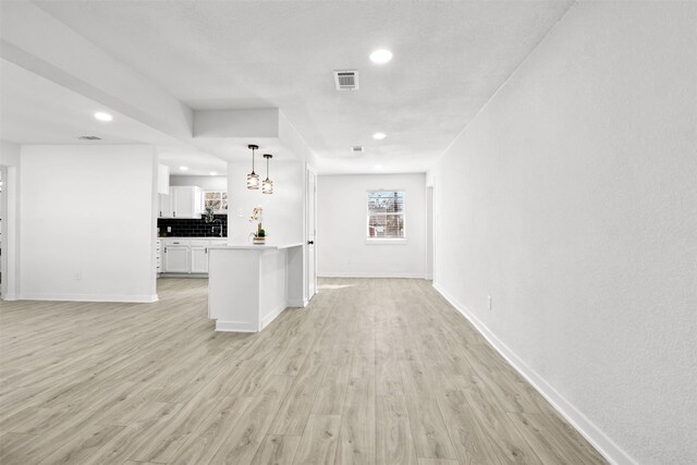 kitchen with backsplash, white cabinetry, hanging light fixtures, and light hardwood / wood-style floors