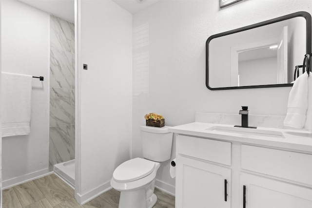 bathroom with vanity, toilet, a tile shower, and wood-type flooring