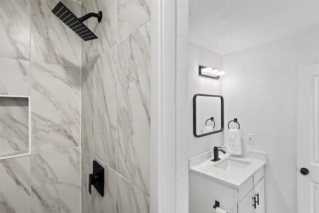 bathroom with tiled shower, a textured ceiling, and vanity