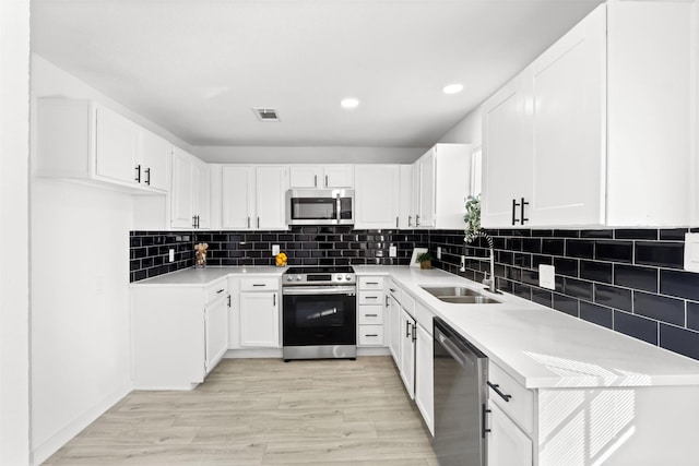 kitchen with appliances with stainless steel finishes, backsplash, sink, white cabinets, and light hardwood / wood-style floors