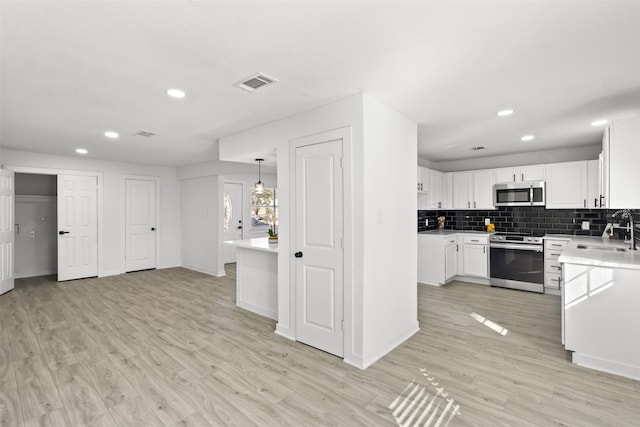 kitchen with white cabinetry, tasteful backsplash, light hardwood / wood-style floors, pendant lighting, and appliances with stainless steel finishes