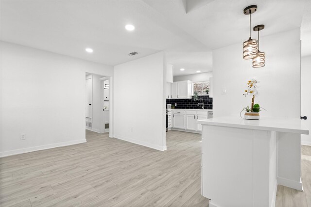 kitchen with pendant lighting, kitchen peninsula, light hardwood / wood-style flooring, decorative backsplash, and white cabinetry