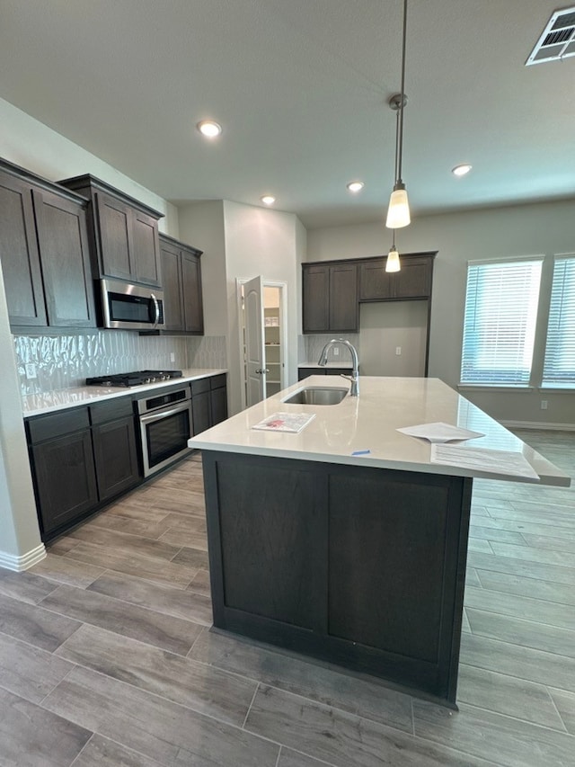 kitchen with appliances with stainless steel finishes, a kitchen island with sink, light countertops, and a sink