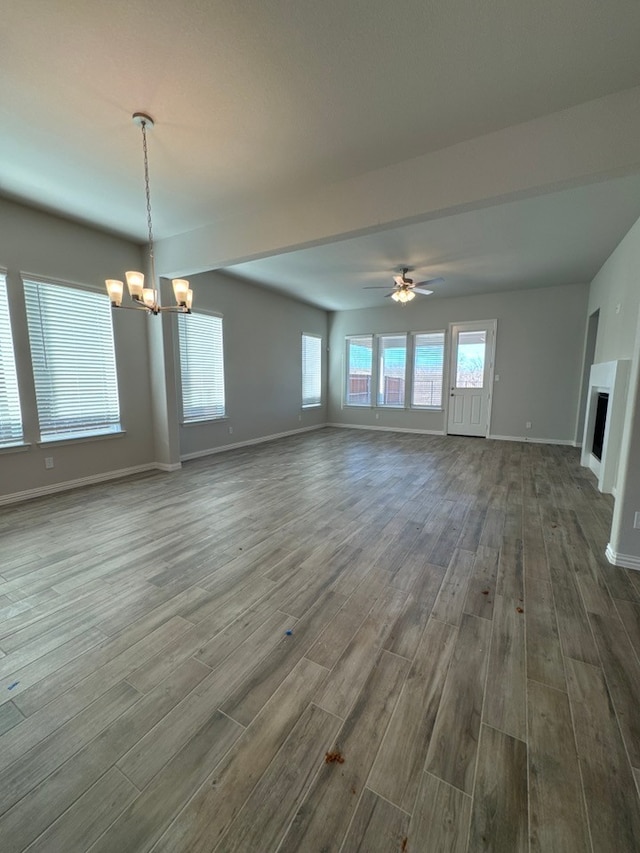 unfurnished living room featuring ceiling fan with notable chandelier, a fireplace, baseboards, and wood finished floors