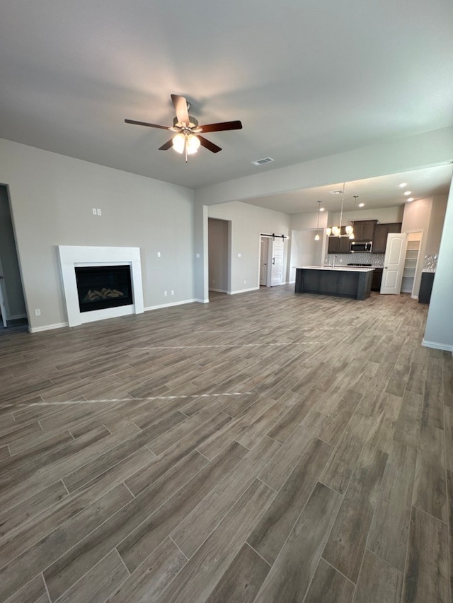 unfurnished living room featuring a barn door, baseboards, dark wood-type flooring, and a ceiling fan