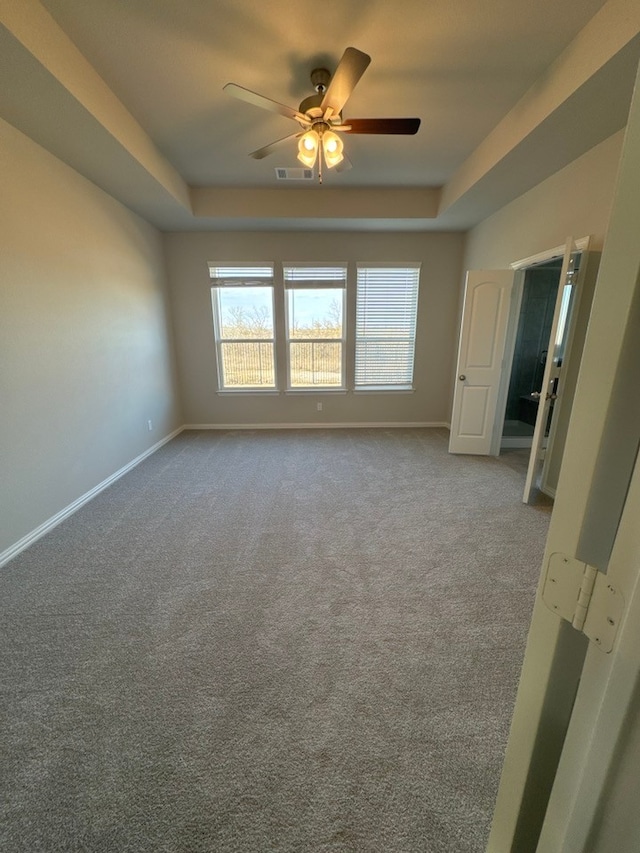 empty room with carpet floors, a raised ceiling, visible vents, and baseboards