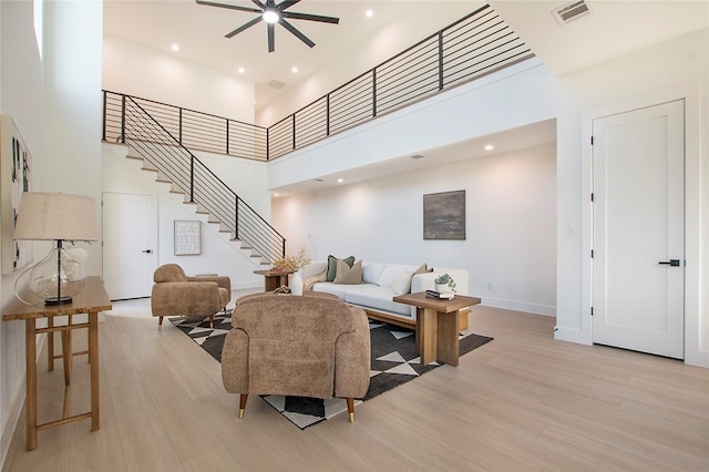 living room with ceiling fan, light hardwood / wood-style floors, and a towering ceiling