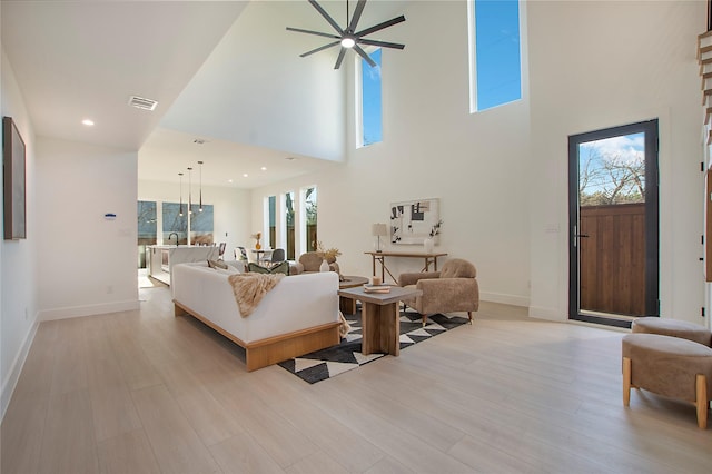 living room with a towering ceiling, light hardwood / wood-style flooring, and ceiling fan