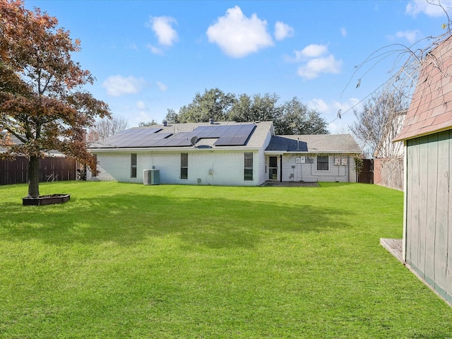 rear view of property with central AC unit, solar panels, and a yard