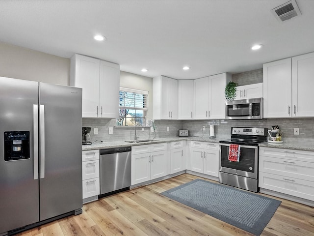 kitchen featuring light stone countertops, appliances with stainless steel finishes, sink, light hardwood / wood-style flooring, and white cabinets