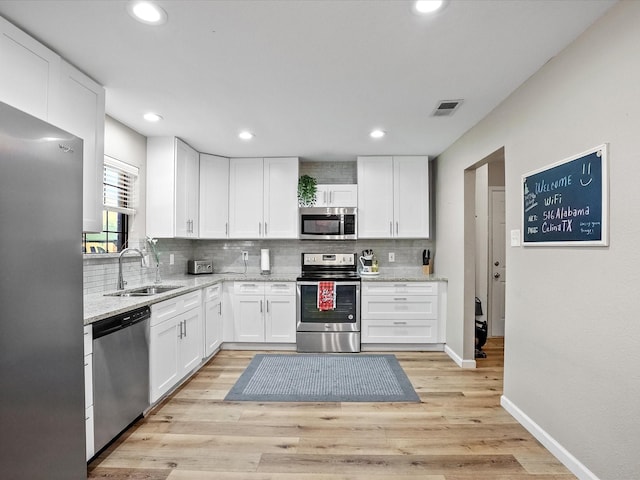 kitchen featuring light stone counters, stainless steel appliances, sink, light hardwood / wood-style floors, and white cabinetry