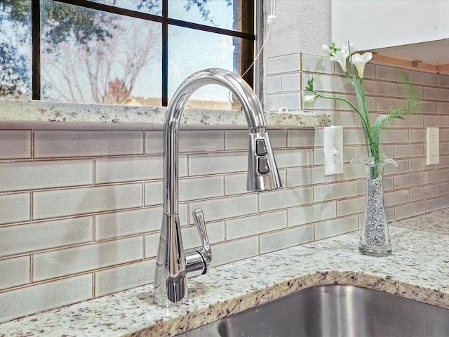 details with backsplash, light stone countertops, and sink