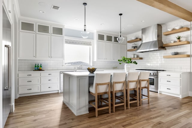 kitchen featuring a kitchen bar, ventilation hood, high end appliances, a center island, and white cabinetry