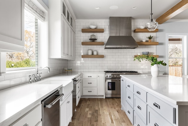 kitchen with white cabinetry, wall chimney exhaust hood, stainless steel appliances, backsplash, and decorative light fixtures