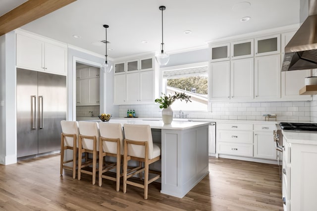 kitchen featuring a center island, high end appliances, ventilation hood, decorative light fixtures, and white cabinetry