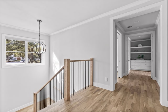 hall featuring a notable chandelier, light hardwood / wood-style floors, built in features, and crown molding