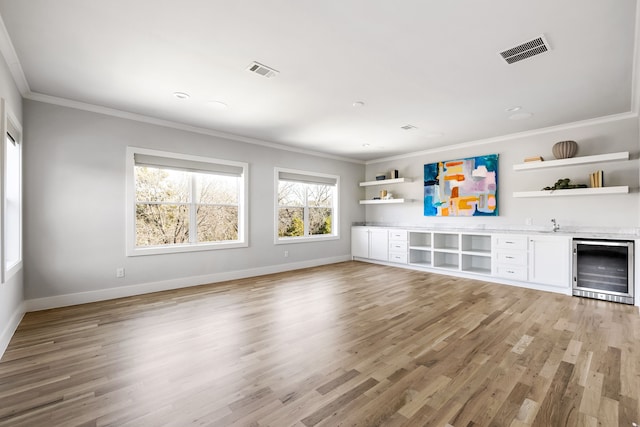 unfurnished living room featuring light hardwood / wood-style floors, crown molding, and wine cooler