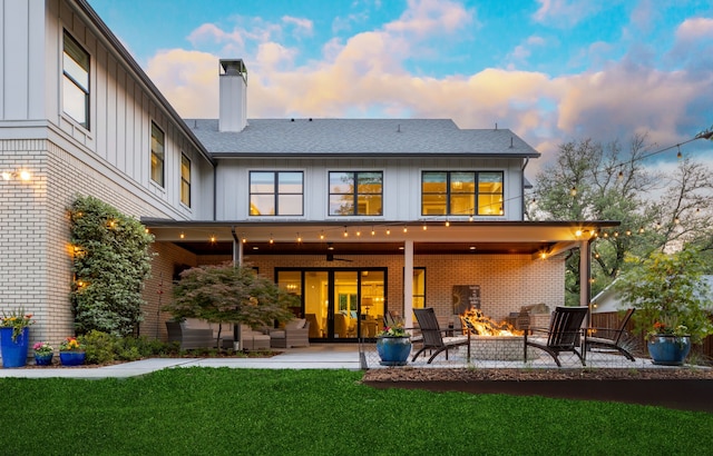 back house at dusk featuring ceiling fan, a patio area, a yard, and an outdoor fire pit