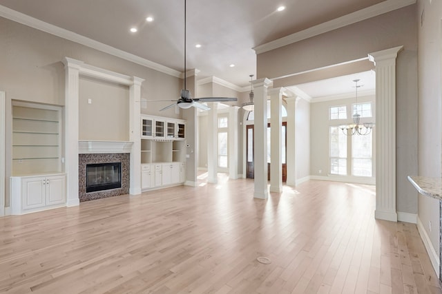 unfurnished living room featuring ornamental molding, built in shelves, ceiling fan with notable chandelier, light hardwood / wood-style flooring, and a high ceiling