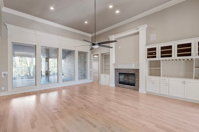 unfurnished living room featuring crown molding, built in shelves, ceiling fan, light wood-type flooring, and a premium fireplace