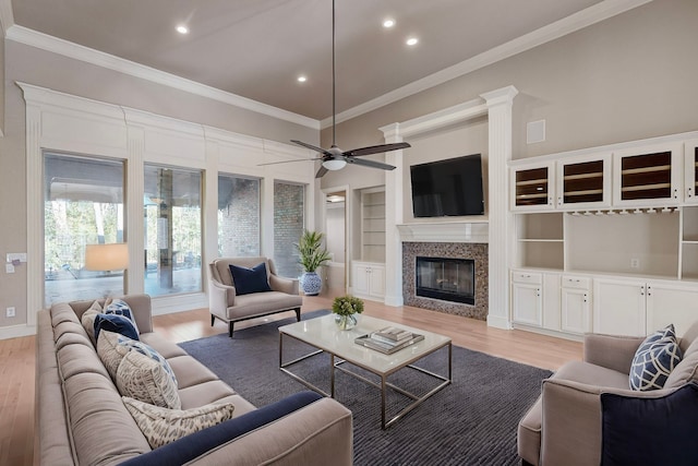 living room featuring a high end fireplace, ornamental molding, built in shelves, ceiling fan, and light hardwood / wood-style flooring