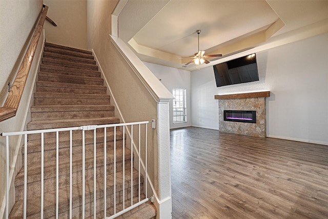 stairs with wood-type flooring, a raised ceiling, and ceiling fan