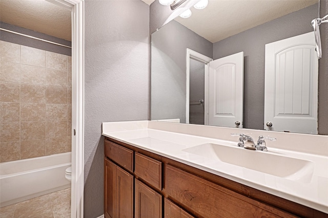 full bathroom featuring tiled shower / bath, tile patterned flooring, vanity, toilet, and a textured ceiling