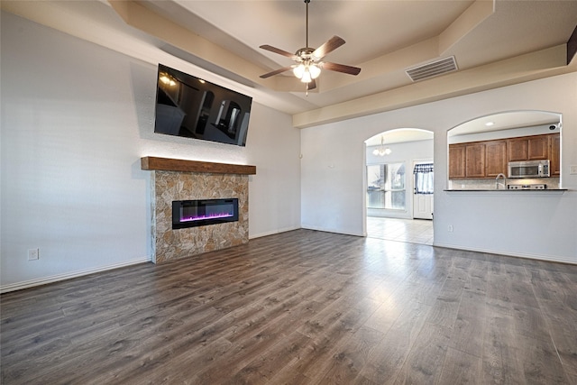 unfurnished living room with ceiling fan with notable chandelier, dark wood-type flooring, a fireplace, and a tray ceiling