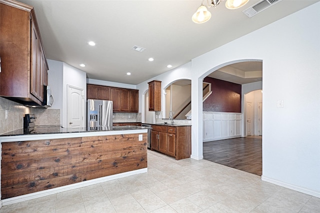 kitchen with pendant lighting, stainless steel appliances, light tile patterned flooring, decorative backsplash, and kitchen peninsula