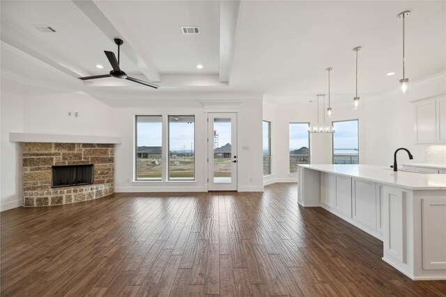 unfurnished living room featuring ceiling fan with notable chandelier, sink, beamed ceiling, a fireplace, and dark hardwood / wood-style floors