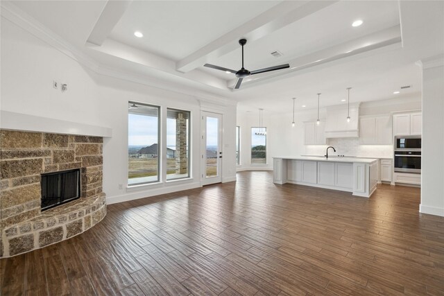 unfurnished living room featuring ornamental molding, ceiling fan, dark wood-type flooring, sink, and a fireplace